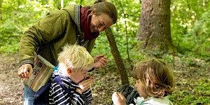 Elisa zeigt zwei Kindern, wie man mit einem Gradhalm pfeift. Elisa und Kinder